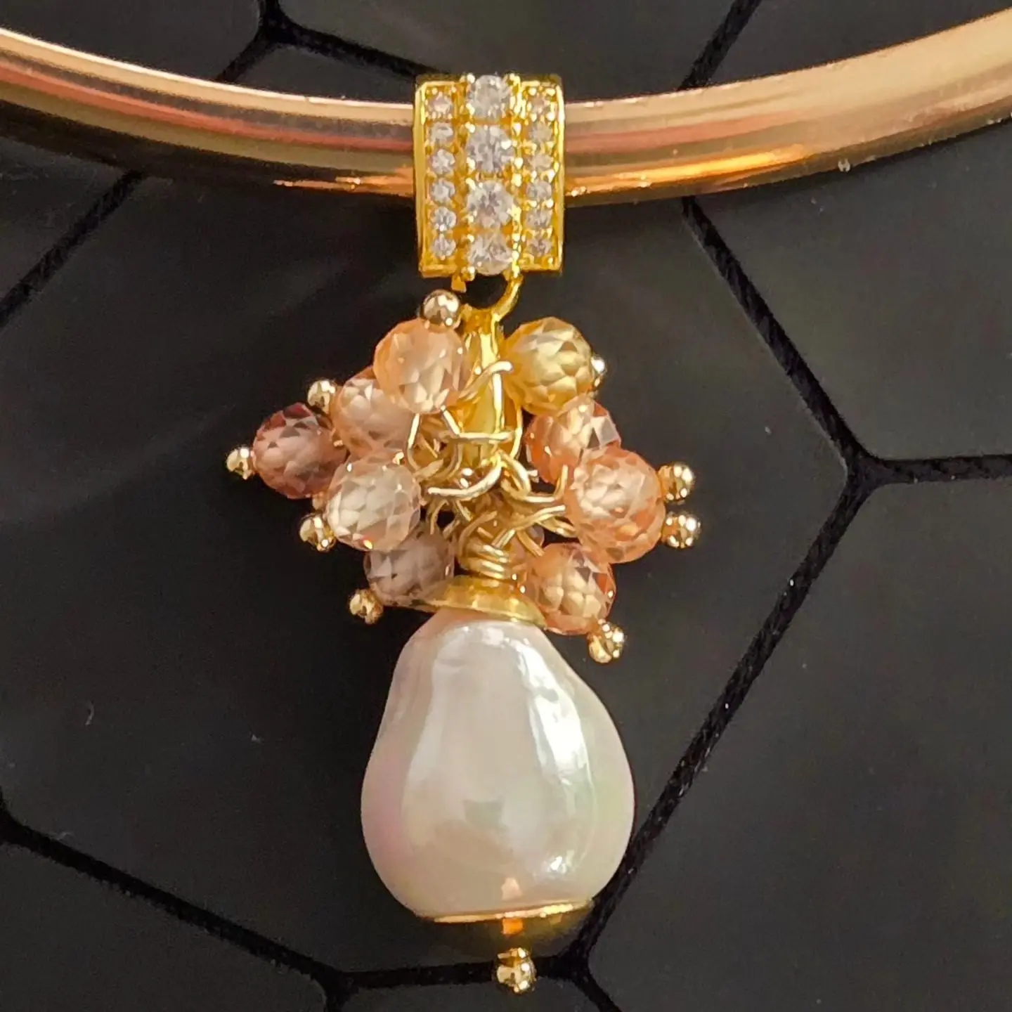 a gold necklace featuring a pendant with a large baroque pearl and a cluster of smaller, light brown beads